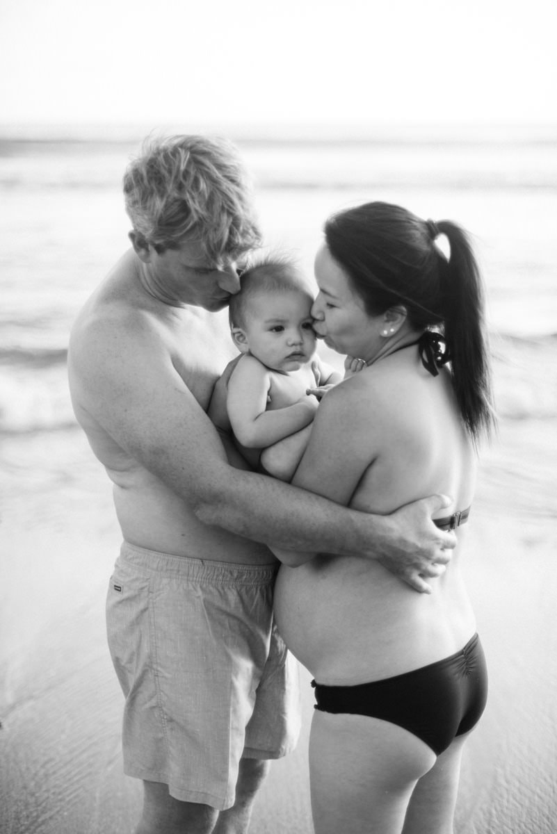 beach maternity photography of mommy dan daddy kissing their lovely son