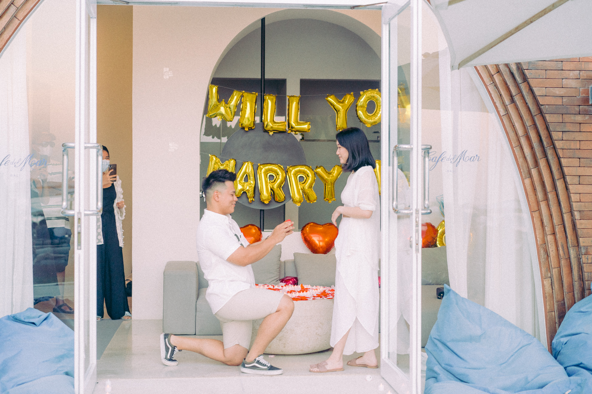 The man down on knee to propose the woman in white outfit on suite room on The couple walk through the entrance pathway on pre-wedding proposal photo session